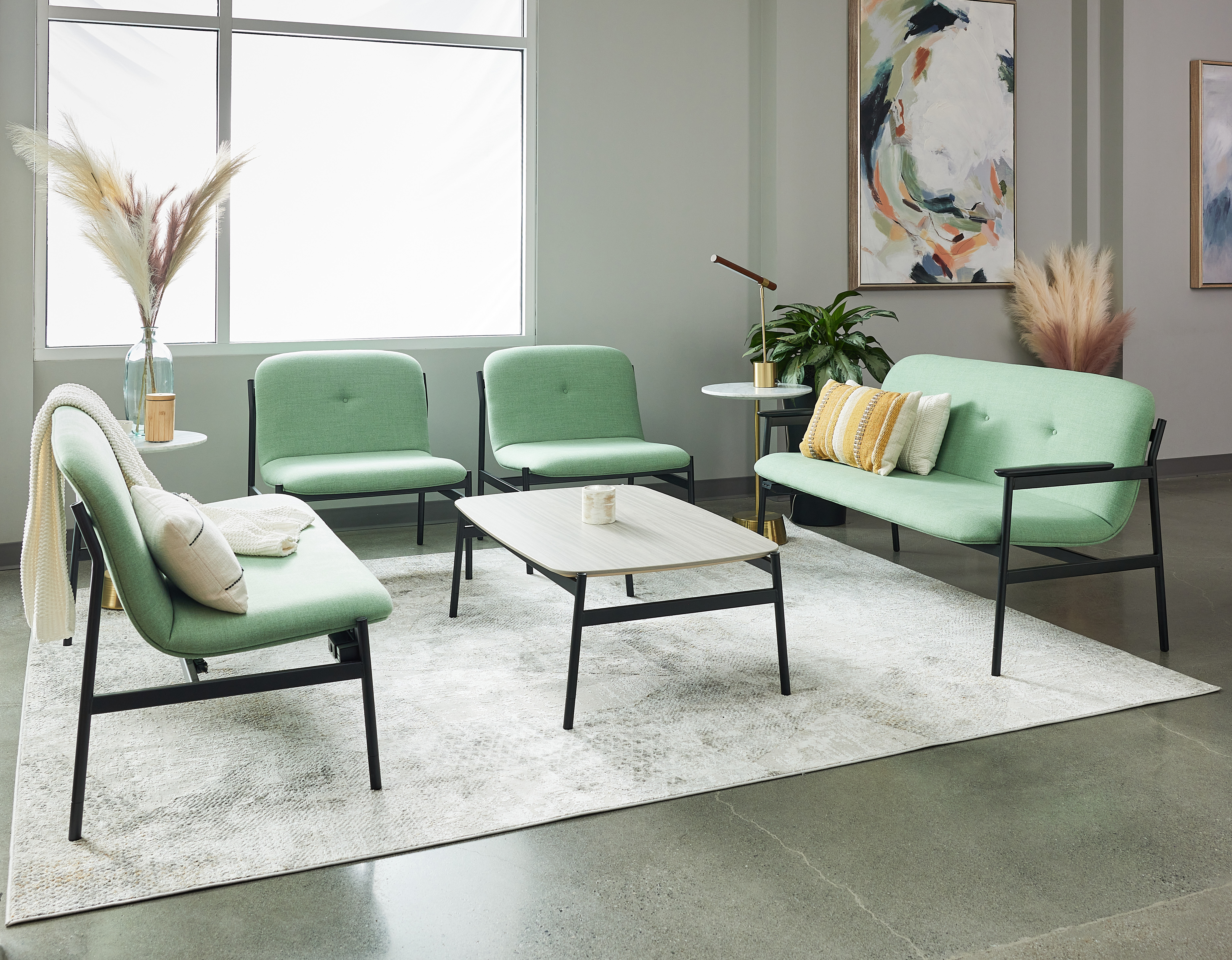 Mint-green upholstered lounge set with sofa and chairs around a light wood coffee table in a modern showroom.