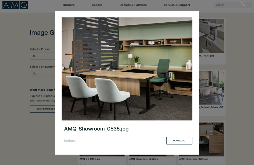 Office showroom: L-shaped wooden desk with a slatted divider, two light-gray chairs, and a green ergonomic chair.