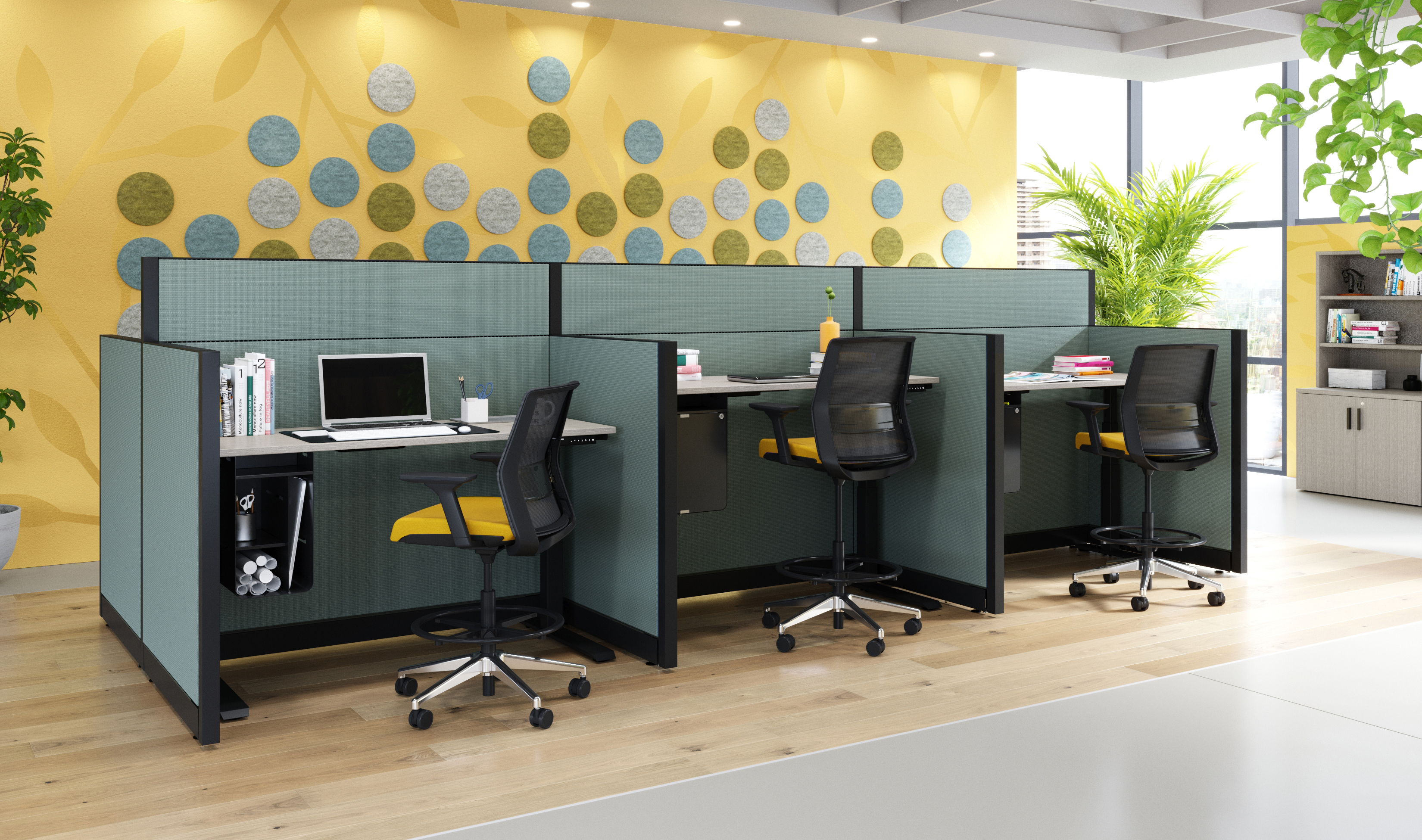 Row of teal cubicles with black-framed partitions and black-and-yellow ergonomic chairs at desks in a modern plant-filled office.